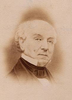 A sepia-toned portrait of the head and shoulders of an older, white haired, balding man wearing a cravat and high collar.