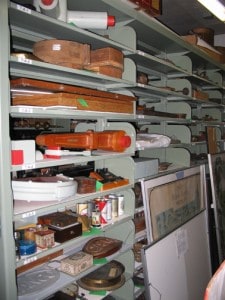 Metal shelving with various items on each shelf like signs, beer cans, wooden containers, and boxes.