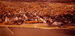 Airborne view of a city on a lakefront showing many buildings and trees, as well as a divided highway along the lakeshore.