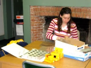 Woman sitting at a table with boxes of slides and a binder to put them in.