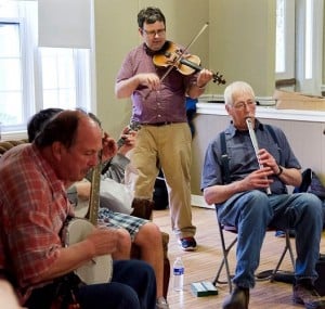 A group of four middle-aged men playing the fiddle, banjo, mandolin and recorder together.