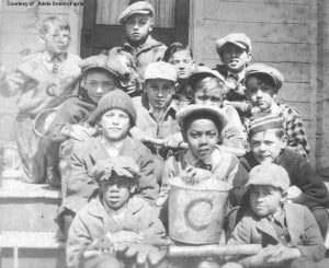 A group of boys sitting on steps wearing caps and holding mitts, a bucket and a bat.