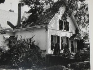 Black and white image of a Gothic style house with two first floor and one second floor window visible on the front.