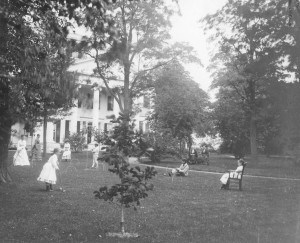 People playing croquet or sitting down in front of a large house
