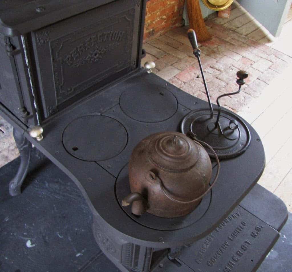 A cast iron tea kettle and coffee roaster on sit an 1850 step stove.