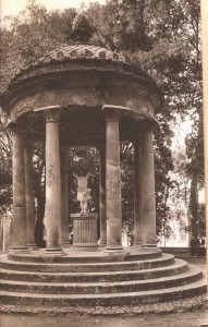 A little girl in a white dress standing with arms lifted on a pedestal under a dome supported by 8 pillars.