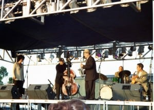 Colored photo of five musicians performing on an outdoor stage.