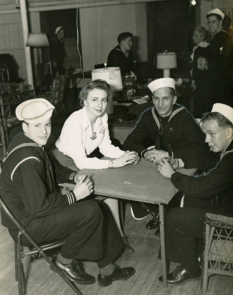 Three sailors sitting at a card table with a young woman.