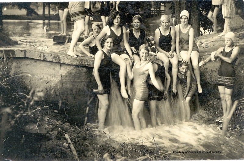 Girls in 1920s bathing suits and caps sitting on the edge of a small waterfall.