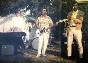 Colored photo of three members of the Tokens. Three men are playing musical instruments outside