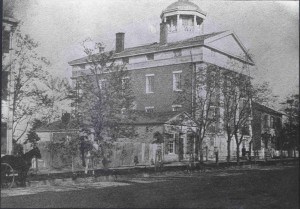 Street view of a large brick building with white columns and a rounded cupola at the top.