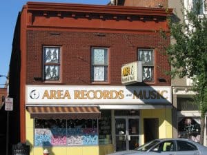 A 2-storey brick building with a sign across the front for Area Records and Music. The windows on all floors are filled with pictures, including silhouettes of a man playing guitar with another man playing saxophone.