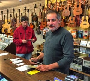 Colored photo of two men standing behind a counter with guitars and cds in the background
