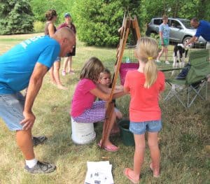 three children milk a fake cow with a man looking on