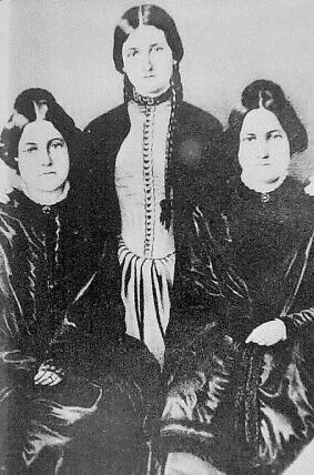 Three young women in old-fashioned dress and hair in buns.