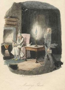 a man sitting in front of a fire place with a man standing next to a table