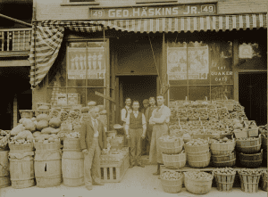 Group of men standing outside a store surrounded by baskets of produce