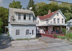 grey multi-story house next to a white multi-story house with a porch