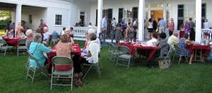 people outside seating at tables or standing on a porch