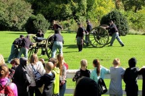 civil war re-enactors firing a cannon while school children look on