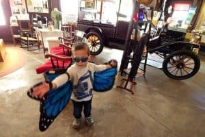 little boy wearing toy butterfly wings with a car in the background