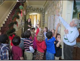 Woman with children in a hallway pointing up to Christmas greenery on the bannister.