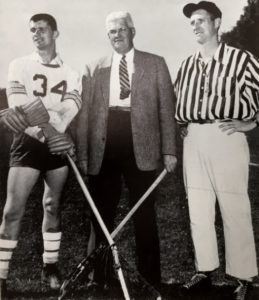 young man in a lacrosse uniform, a man in a suit and tie and a referee