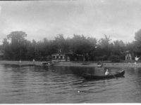 man in a canoe with people, canoes and four houses along the shore line