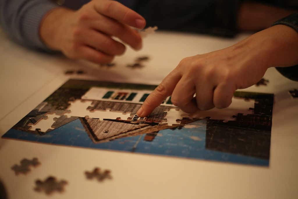 Hands putting together a jigsaw puzzle of a house