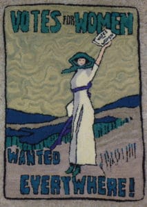 Hooked rug showing a woman with her hand in the air holding a Votes for Women flier. Wanted Votes for Women is witten on the rug.