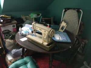 A table with sewing machine, iron, sewing materials and masks on it.