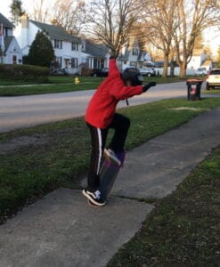 Boy doing an ollie on a skatboard on the sidewalk of a suburban street.