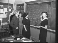 woman pointing at writing on a chalkboard with writing on it with three adults looking on