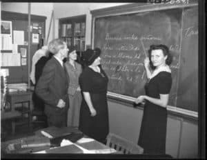 woman pointing at writing on a chalkboard with writing on it with three adults looking on 