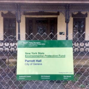 Green Sign on a fence in front of a Yellow Brick Building