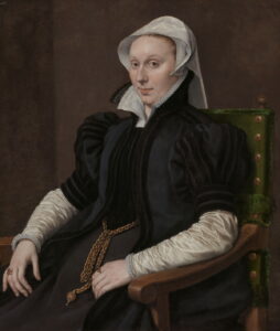 Portrait of a seated woman in stiff black velvet bodice, skirt and jacket. She also has on an upright collar and silk blouse and cap.
