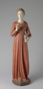 Wooden statue of a woman in a long-sleeved orange gown belted at the waist.