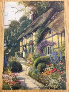 English cottage surrounded by flowers and shrubs with a woman at the front door