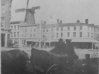 A wagon with a downtown intersection and grist mill in the foreground