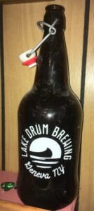 Brown glass bottle with "Lake Drum Brewing Geneva, NY" and an image of a canoe in the water printed on it.