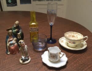 Two tea cups, from my grandmother, a glass, a Napco figurine, a statue of the Holy Family, a bottle and a champagne flute