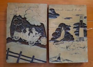 two printing blocks.  One contains an automobile with two people.   The other is a sailboat on the water with a lighthouse
