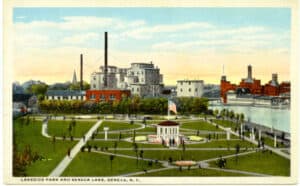 Postcard image of people in a lakeside part with factories in the background