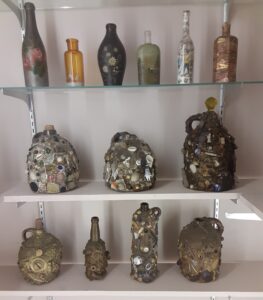 One shelf has painted bottled and two shelves have memory jugs