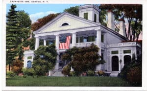 Color postcard photo of a Greek Revival building with a two-storey, four-columned pediment with an American flag hanging from it.