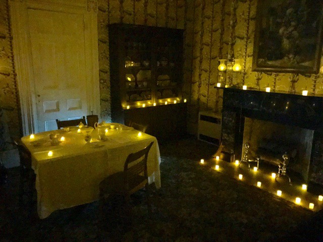 A room with a set table with chairs, a china cabinet and fireplace mantel covered with votive-size candles.