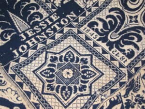 Detail of a blue and white coverlet with Jessie Johnston 1845 around a floral element.
