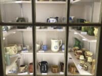 A cabinet with four rows of shelves containing ceramic pitchers of all types and sizes.