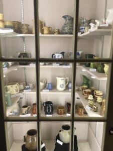 A cabinet with four rows of shelves containing ceramic pitchers of all types and sizes.