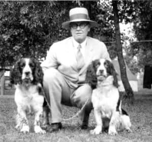 A man kneeling with two dogs on either side of him
